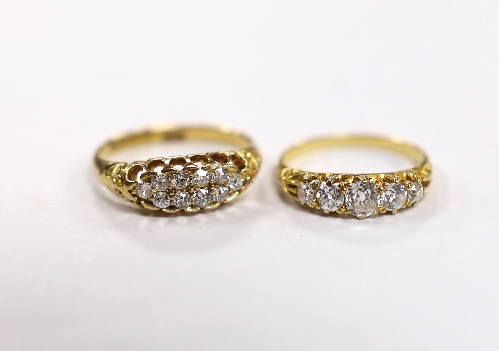 An Edwardian 18ct gold and two row diamond cluster set half hoop ring, size L and a yellow metal and graduated five stone diamond set half hoop ring, size H, gross weight 4.8 grams.